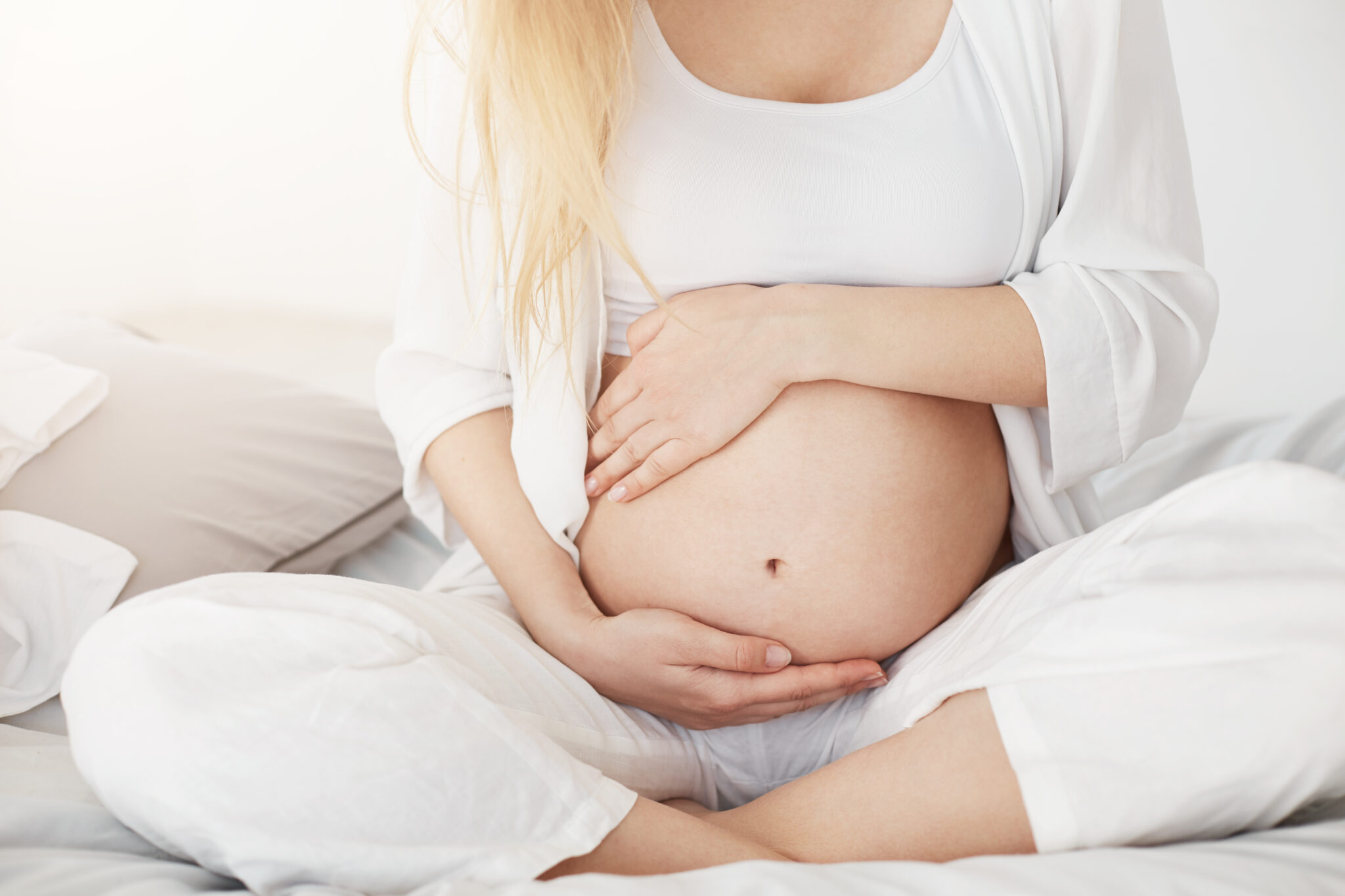 Historie, które krzepią young pregnant soon to be mother touching her belly sitting in her bedroom in afternoon. pregnancy concept. high key.